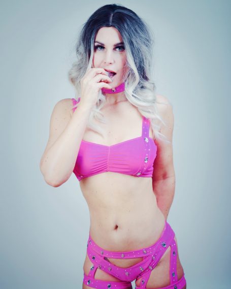 Frau in pinkem knappen Outfit mit langen, hellen Haaren, posiert verführerisch.